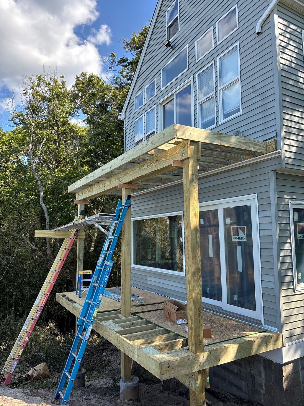 White-framed window on blue siding beside exposed plywood construction and a ladder on the right.