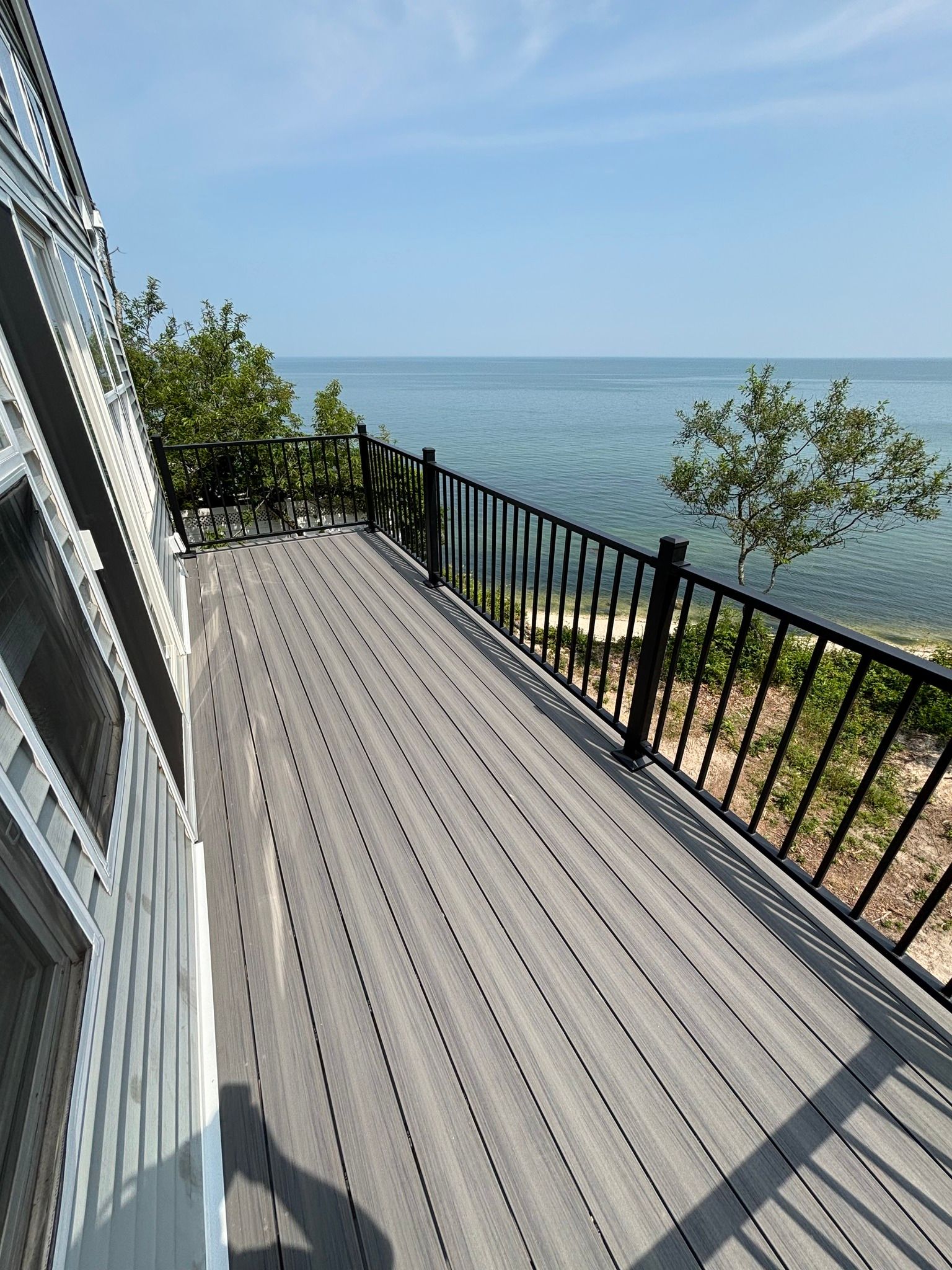 Deck overlooking the ocean with black railing, trees, and a blue sky.