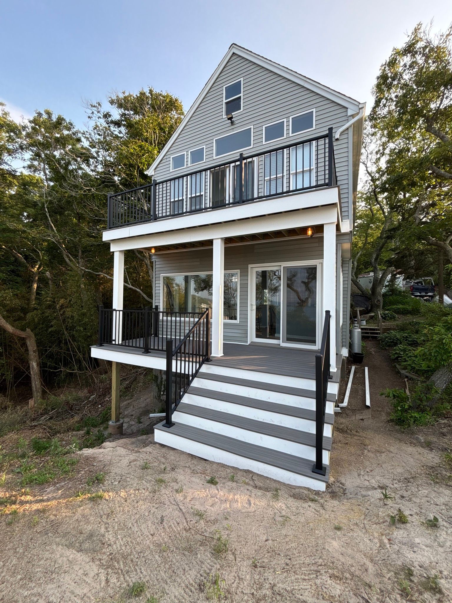 Gray beach house with striped front steps, porch, and balcony surrounded by trees.