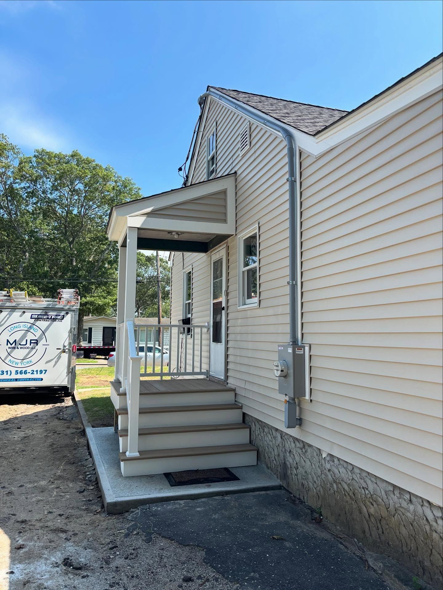 Small beige house entrance with front steps, white railing, and a covered porch ramp area.