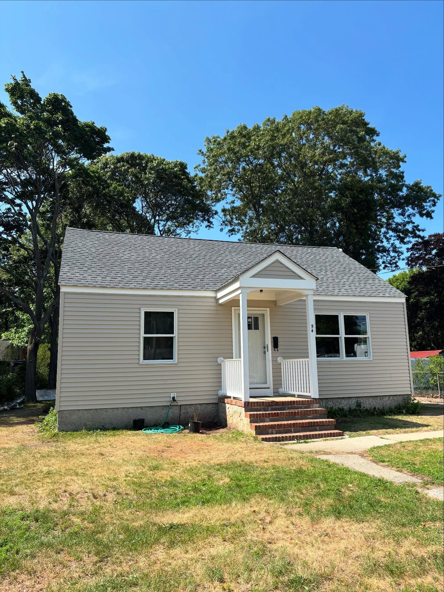 Small white house with a front porch, red steps, and a grassy yard under trees