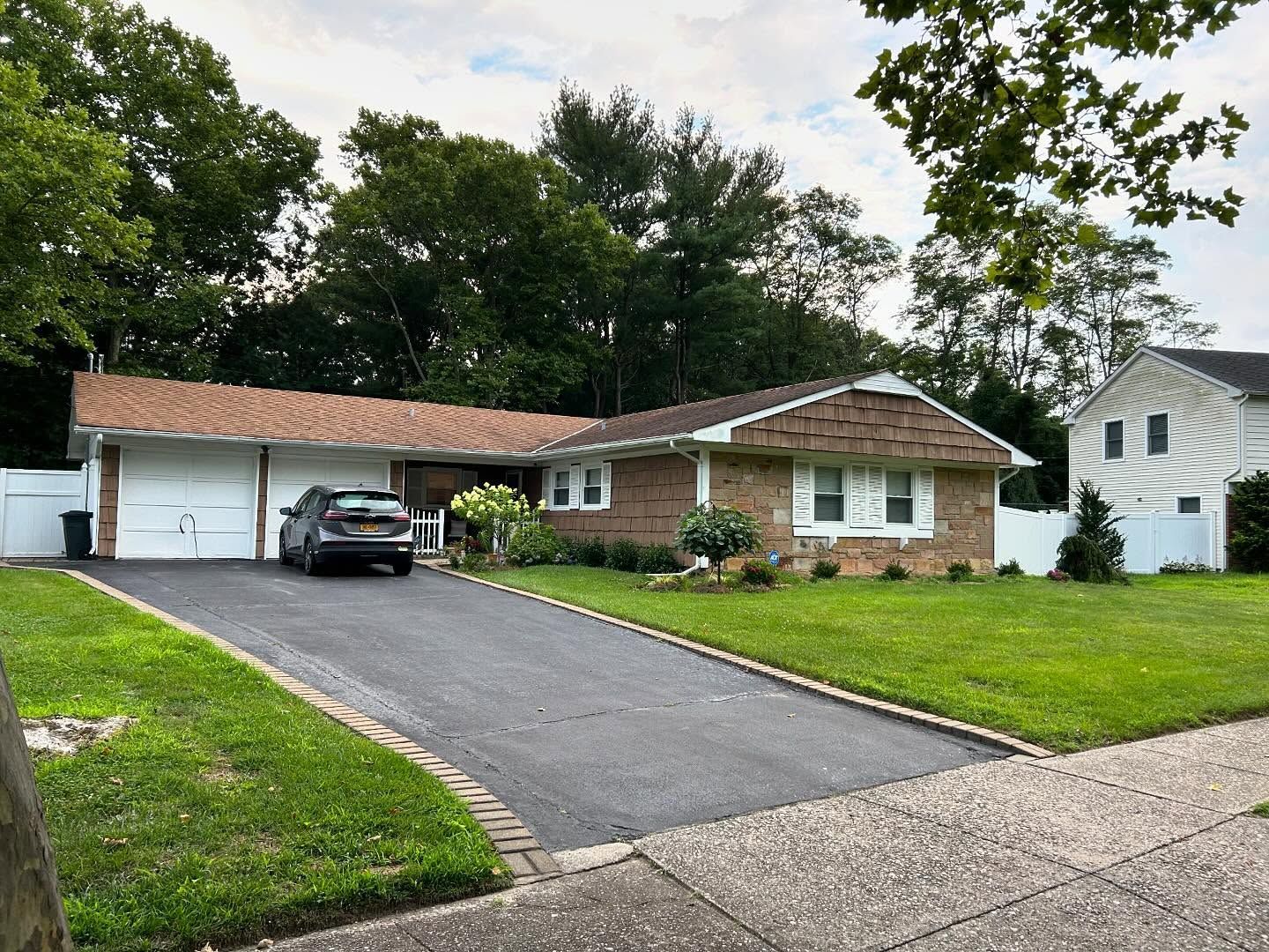 Single-story brick house with driveway, black car, and green lawn under cloudy sky