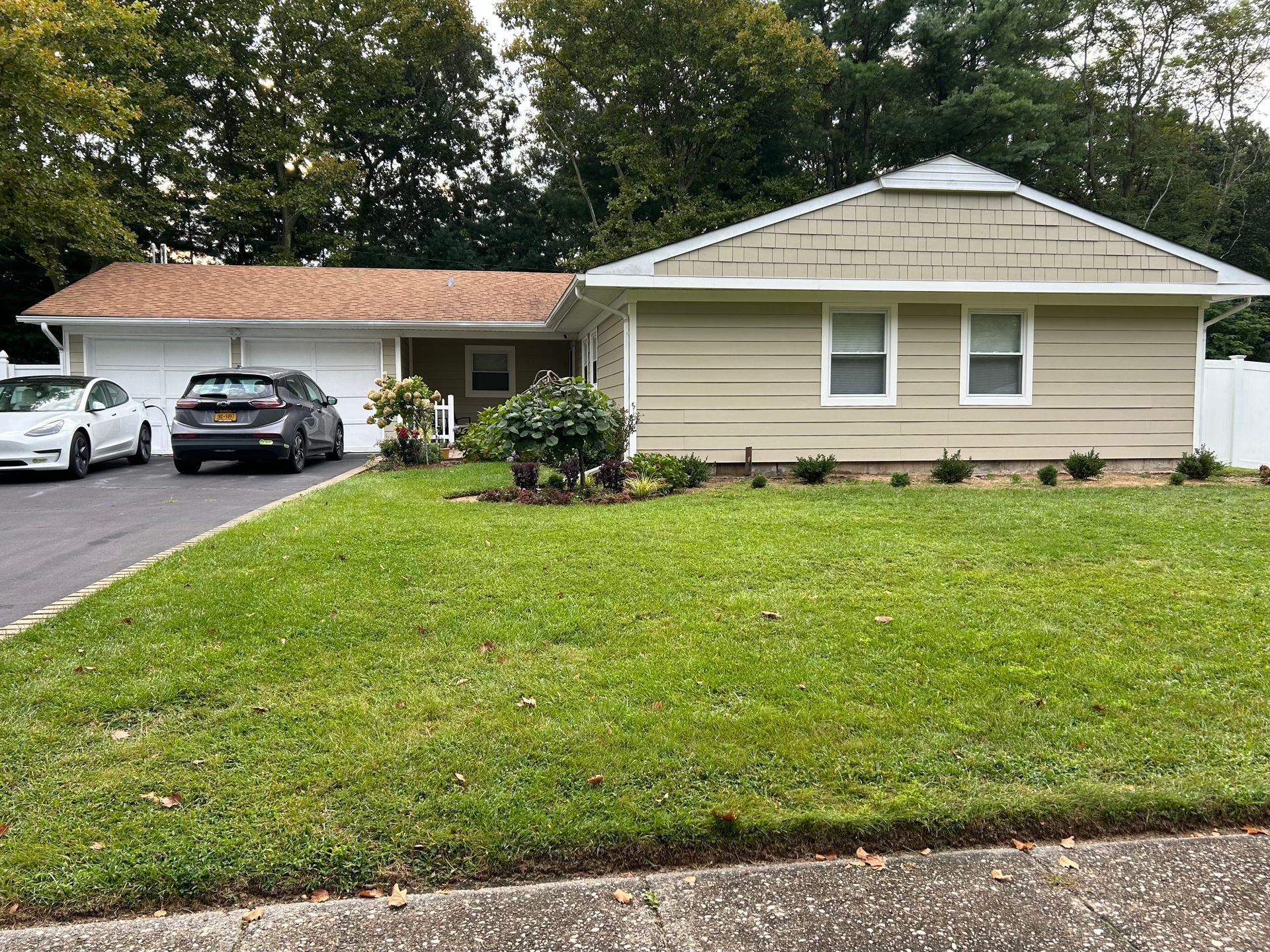 Single-story beige house with carport, two parked cars, and a large green front lawn.