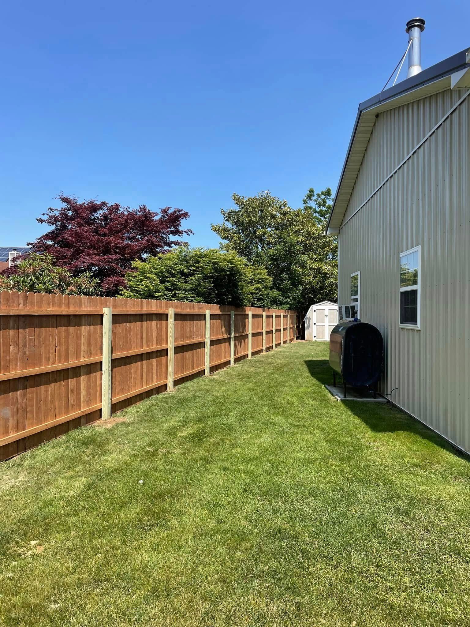 Backyard with green lawn, wooden fence, and beige house under a clear blue sky