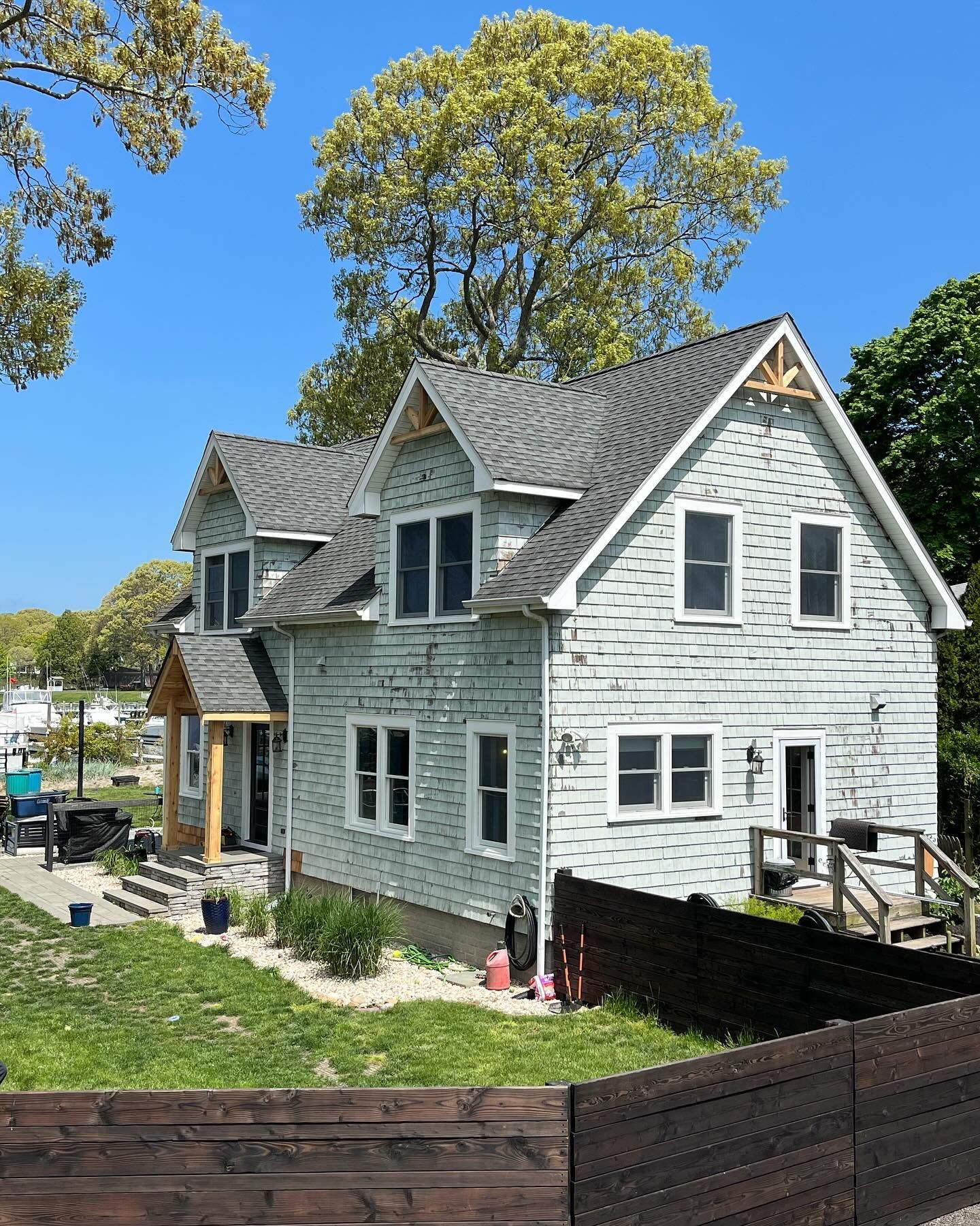White two-story house with gray roof and black fence in a sunny yard, seen from the front-left.