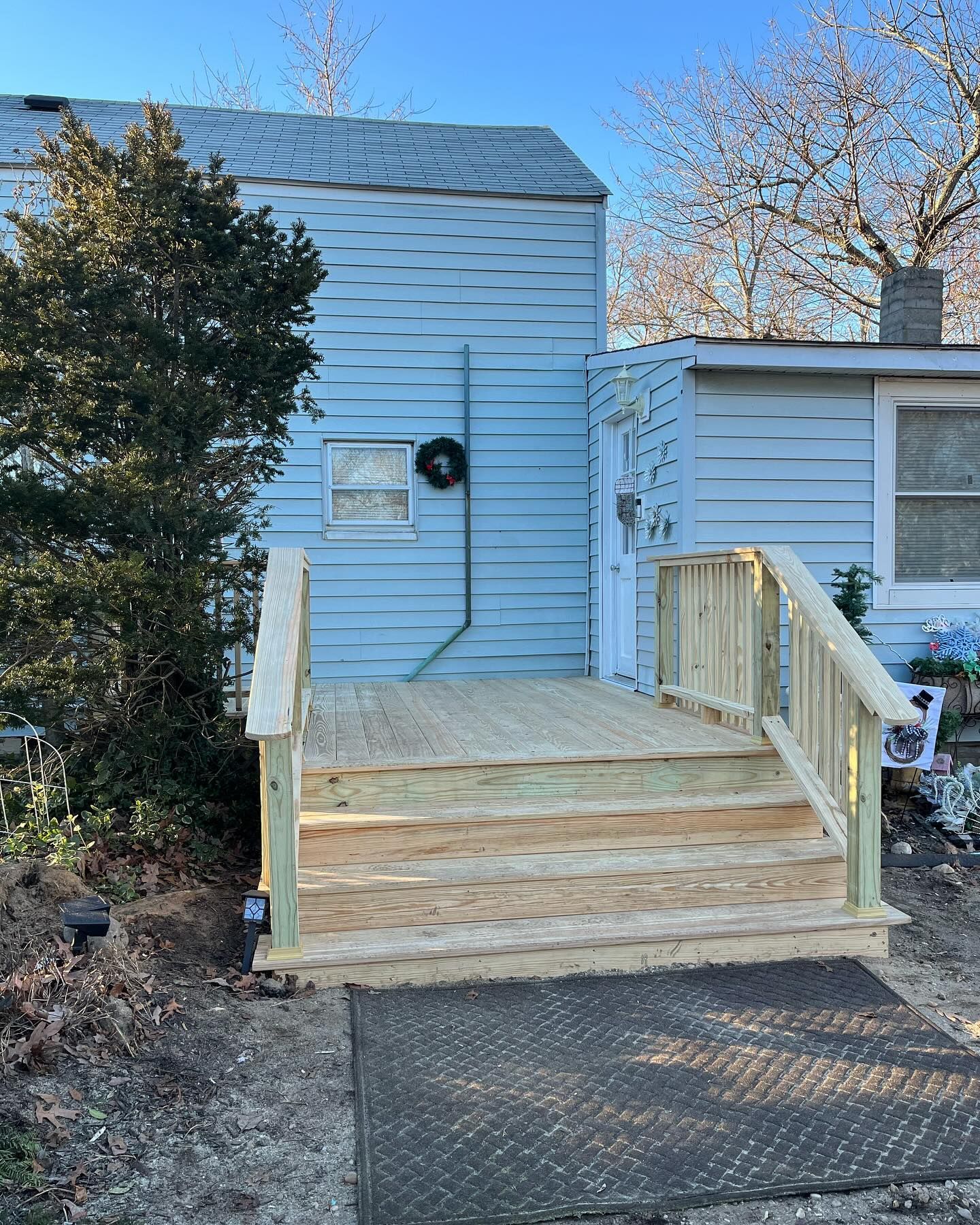Wooden wheelchair ramp with railings leading to a white house entrance in a yard