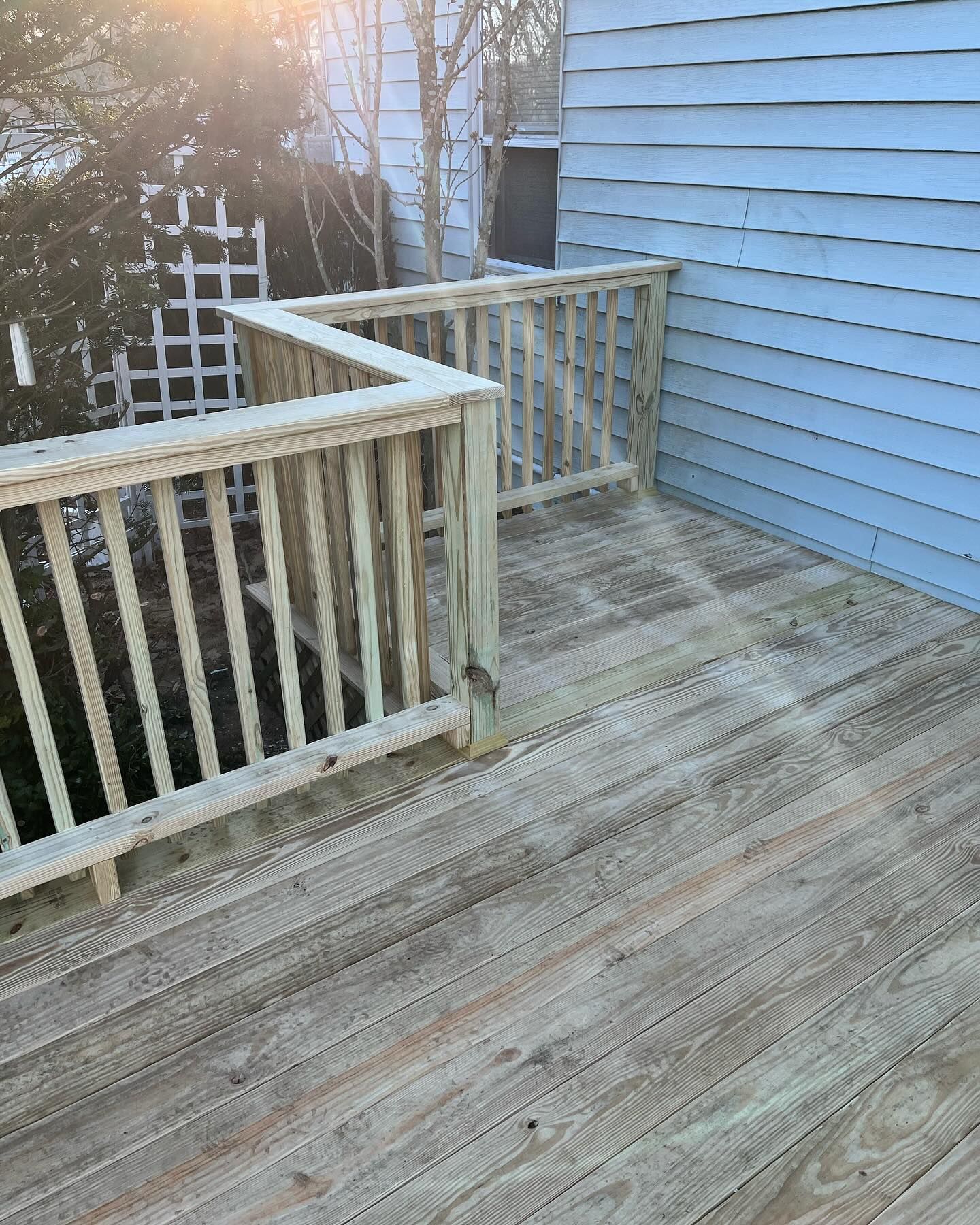 Weathered wooden deck with white railings beside a blue house, lit by low sunlight.