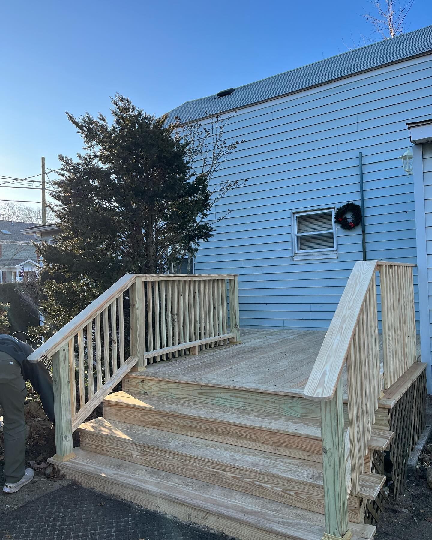 Wooden front steps and railing leading to a blue-sided house with a small deck in a snowy yard.