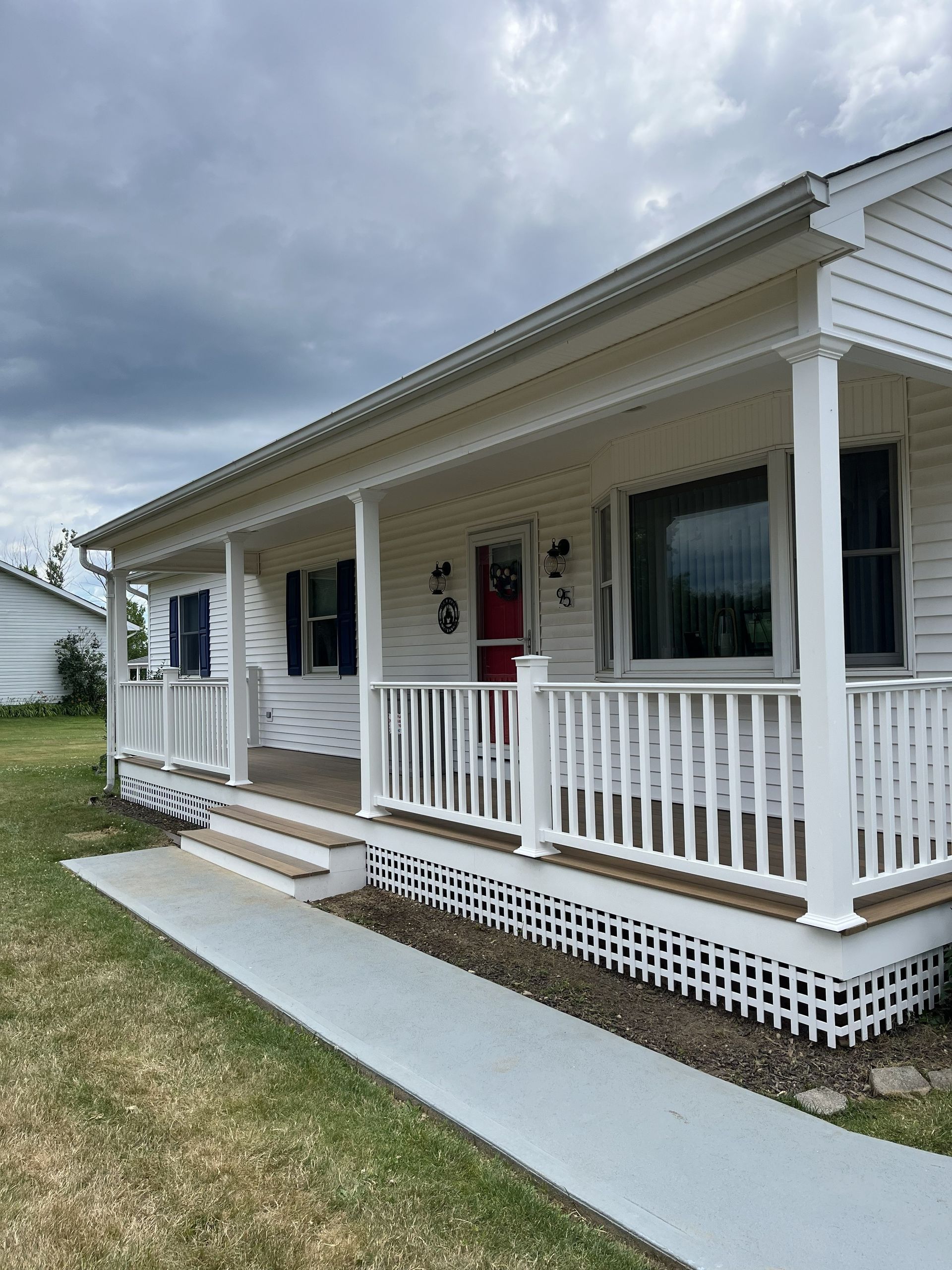 White single-story house with a covered porch, white railing, and cloudy sky overhead.
