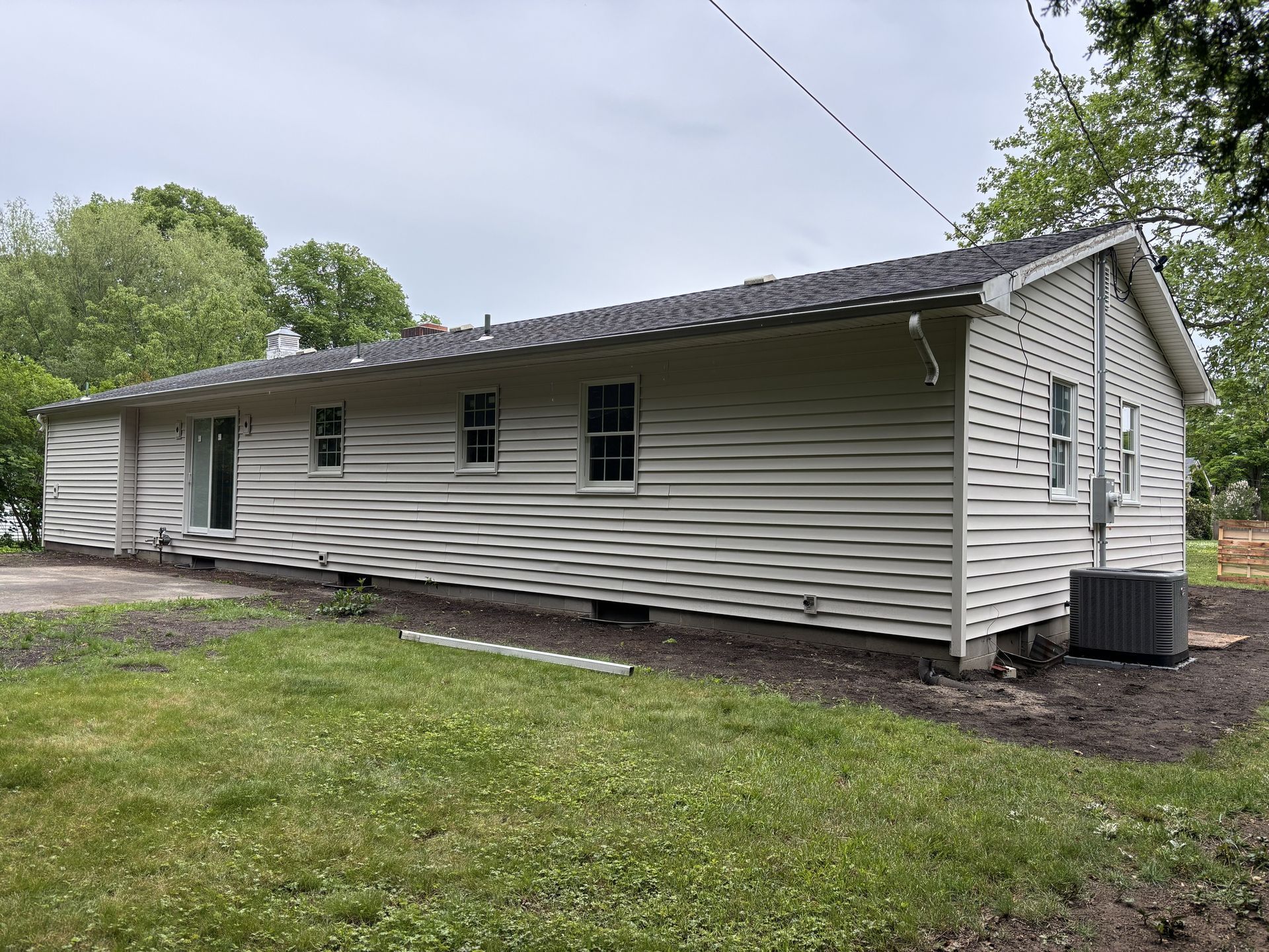 Single-story white house with dark roof and siding, shown from the side in a grassy yard.