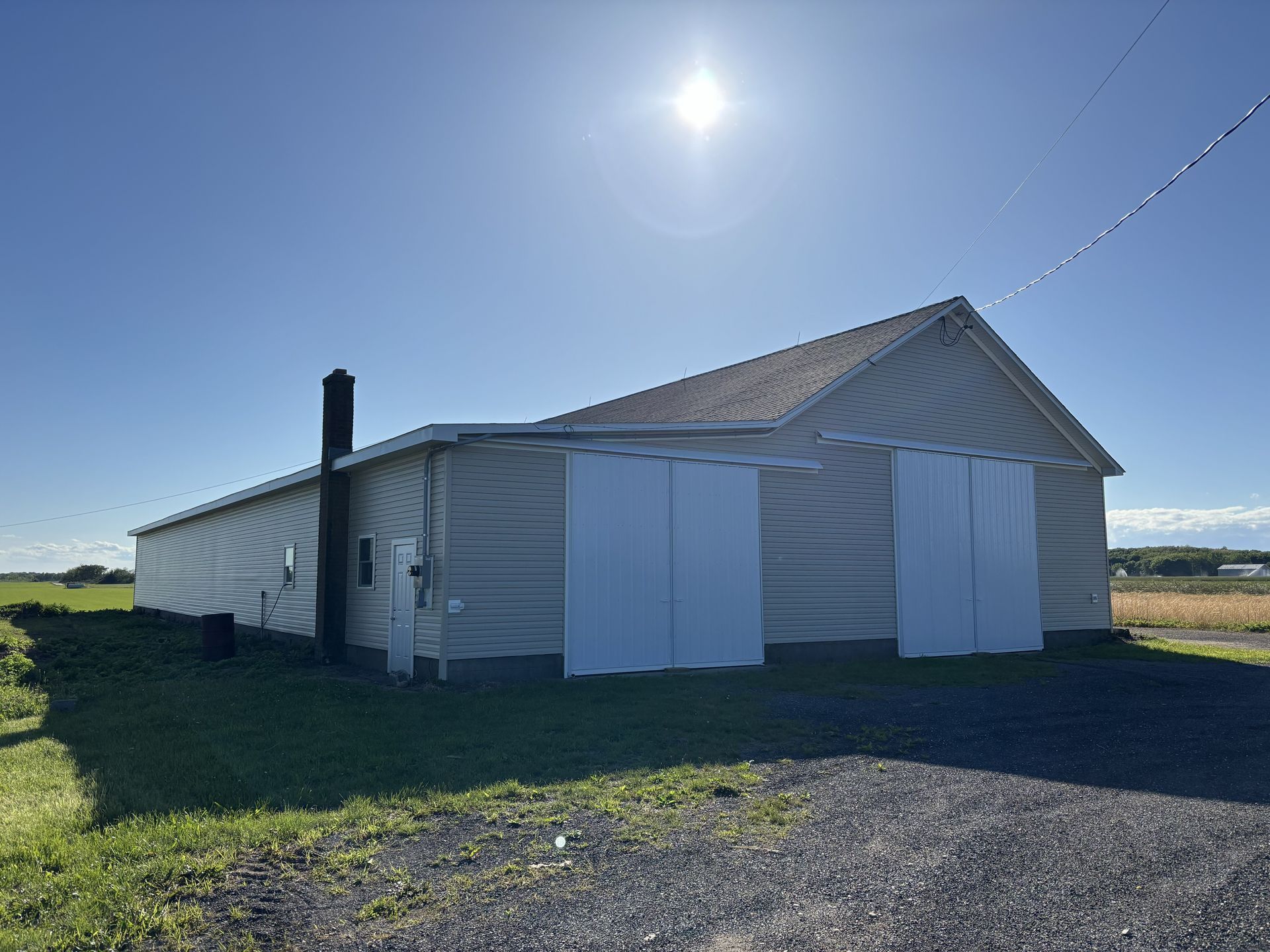White farmhouse with closed shutters on a sunny rural lot under a clear blue sky.