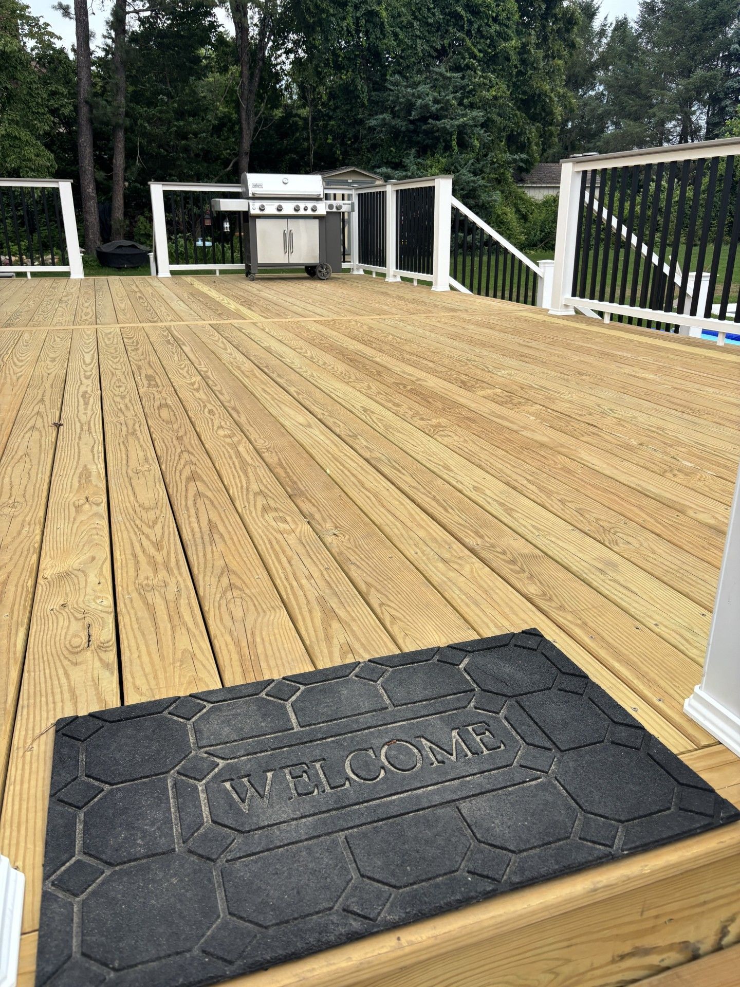 Wooden deck with white railing and a black doormat at the entrance.