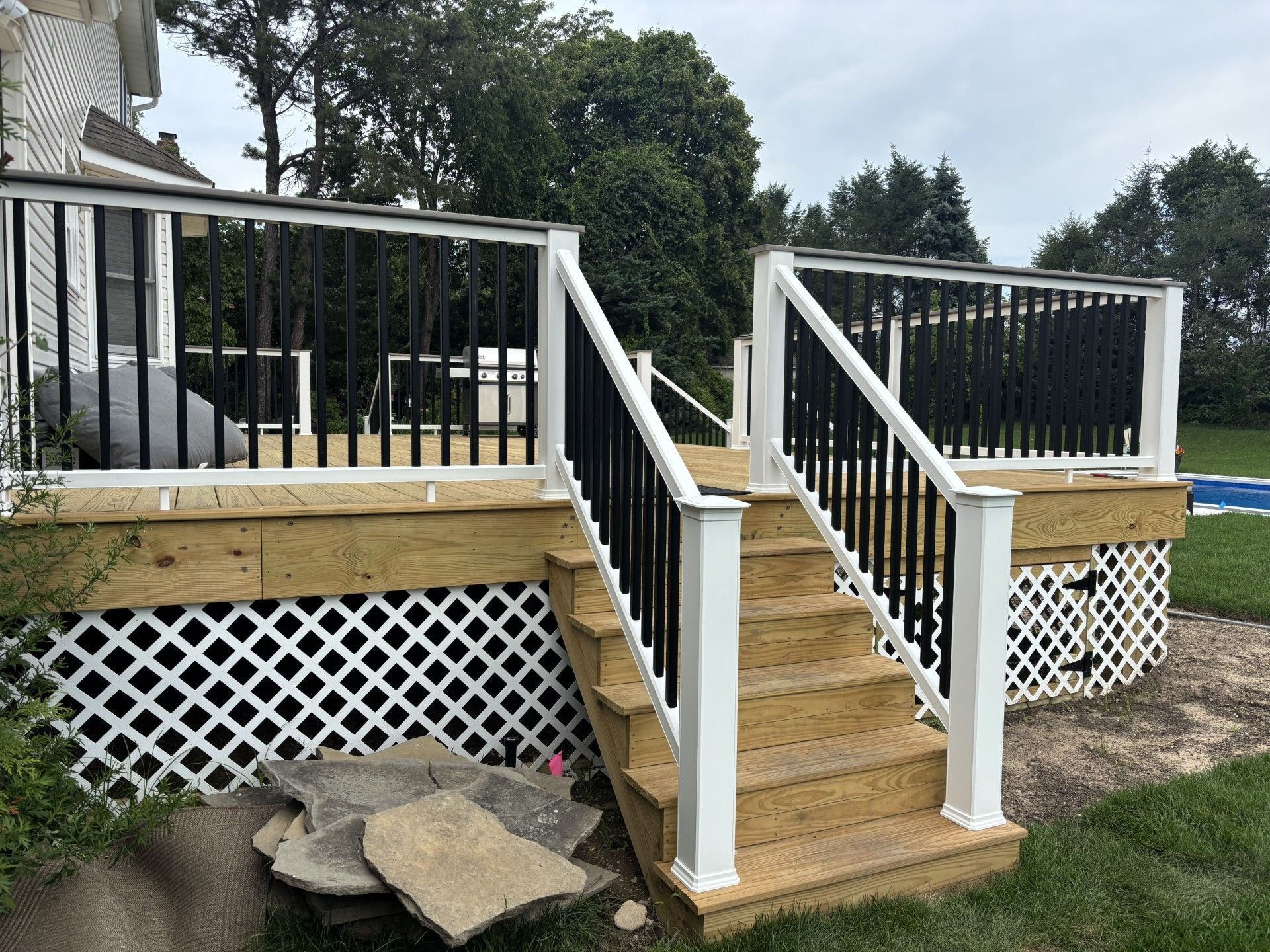 Wooden backyard deck steps with white railings and lattice skirting beside a house.