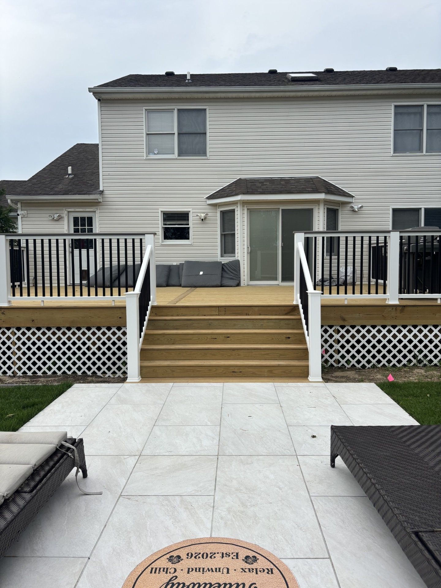 Backyard patio with white pavers, steps, deck railings, and a two-story house in the background