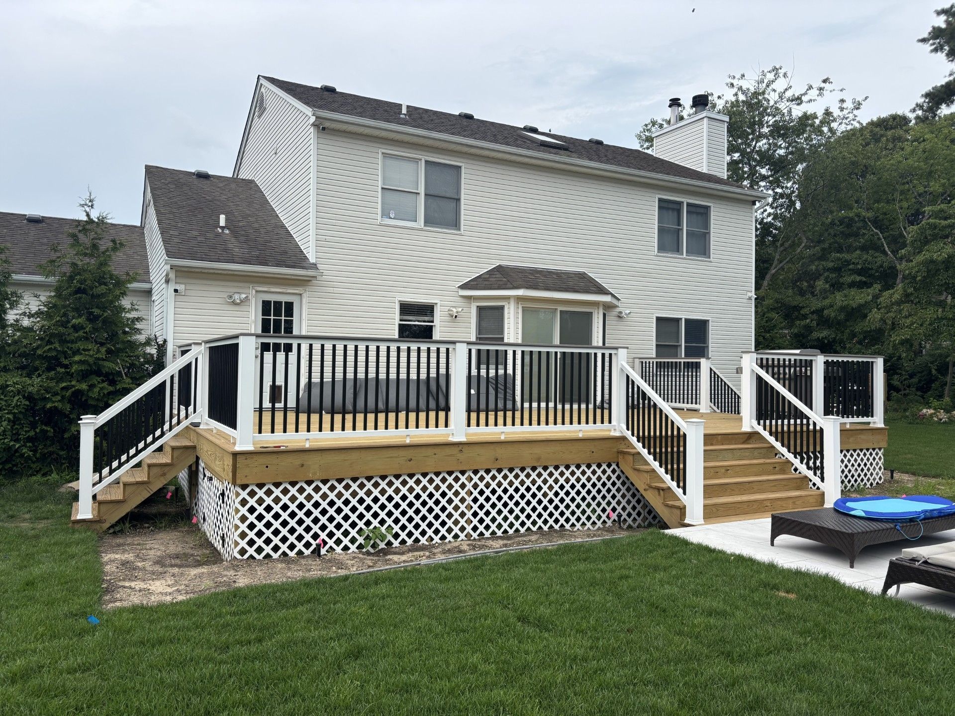 Two-story white house with a large wooden deck and stairs leading to a grassy yard