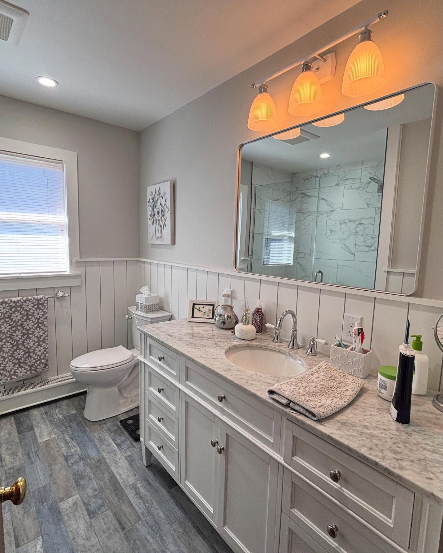 Elegant bathroom with gray vanity, marble countertop, large mirror, and warm pendant lights