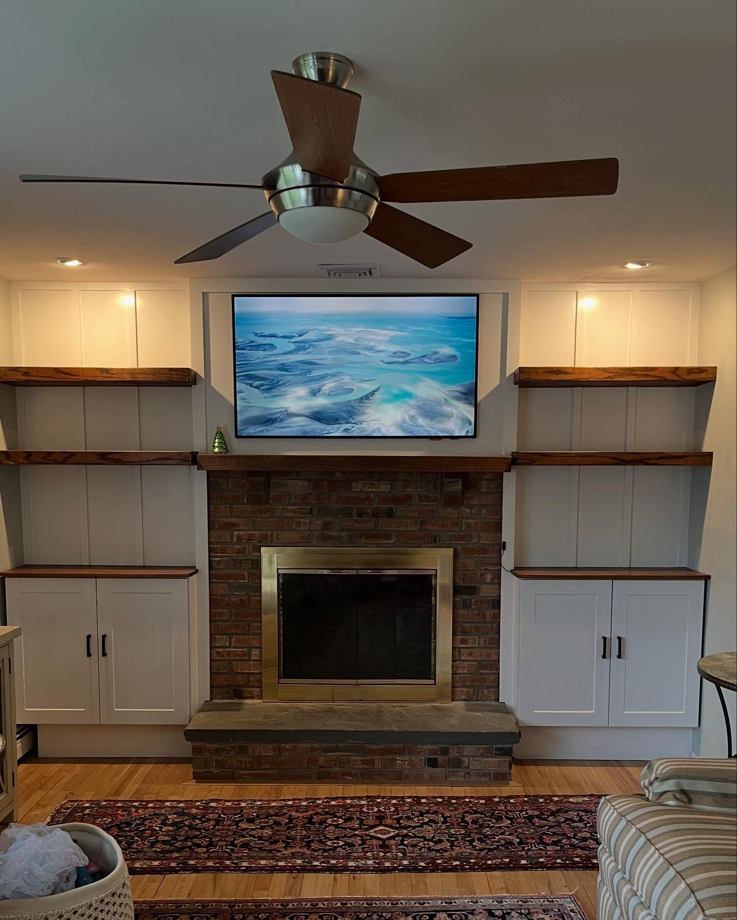 Living room with fireplace, built-in shelves, mounted painting, and ceiling fan over a patterned rug