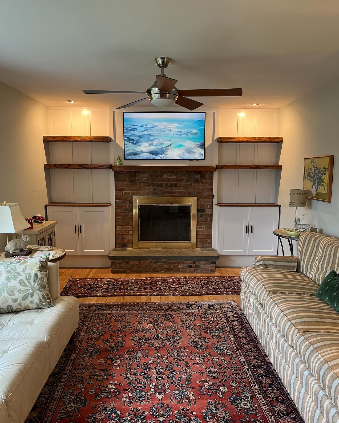 Living room with fireplace, built-in shelves, red patterned rug, and wall-mounted TV above mantel.