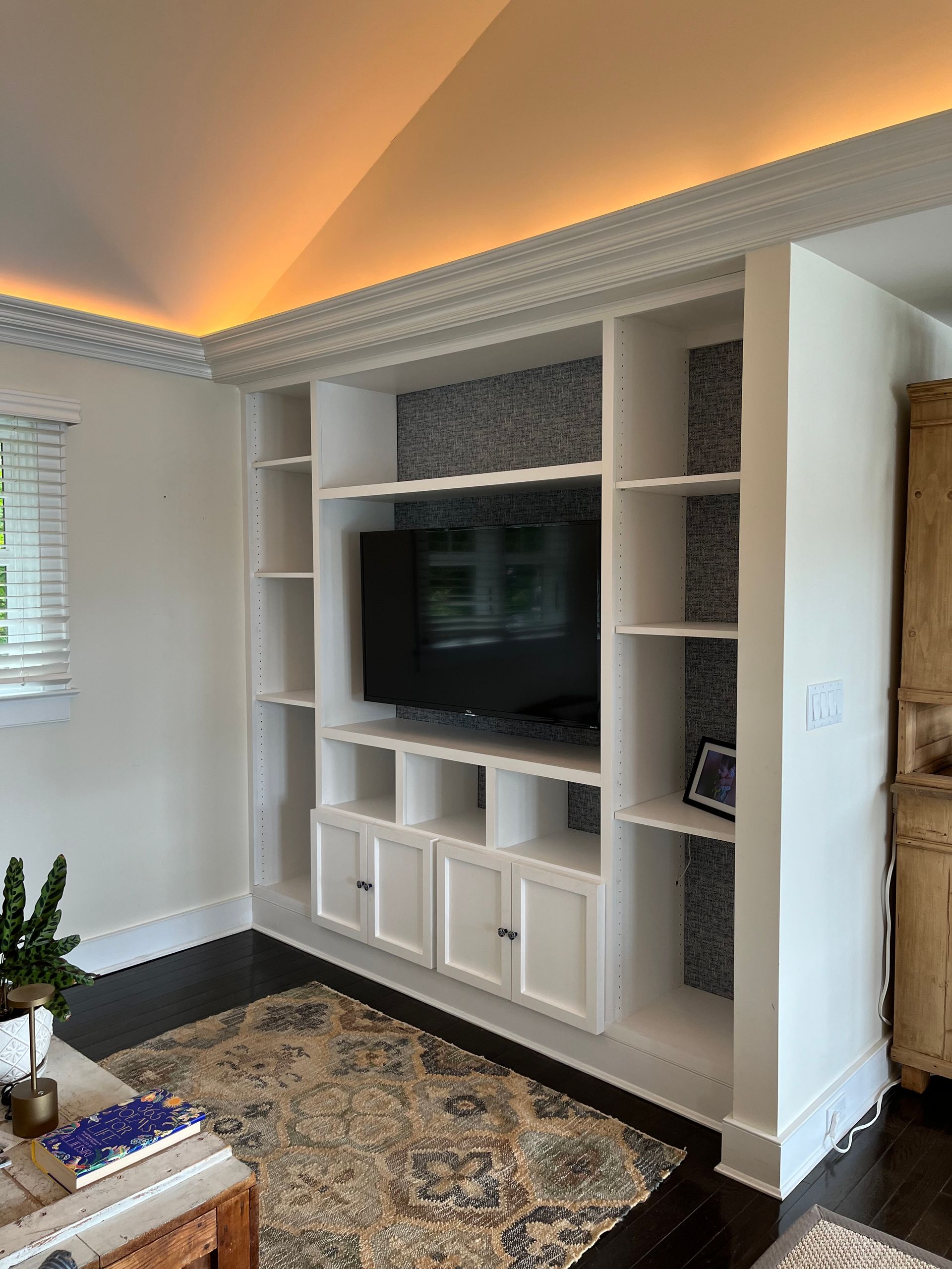 Built-in living room TV wall with shelves, white cabinetry, and warm cove lighting