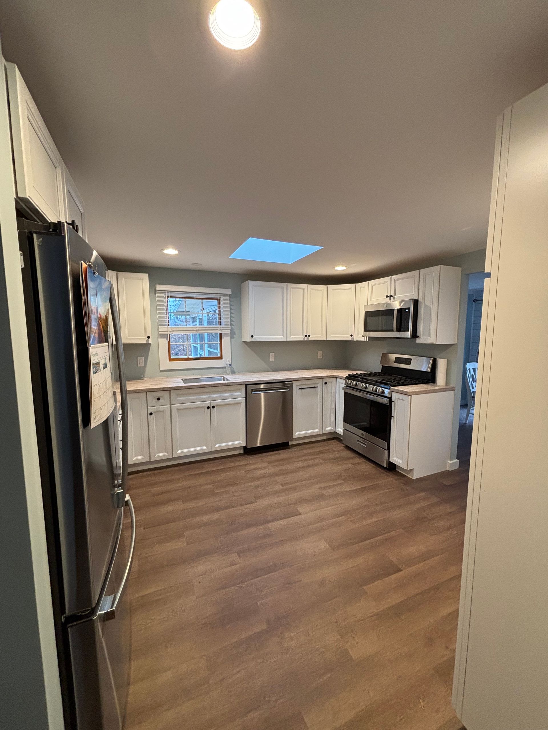 Small kitchen with white cabinets, stainless fridge, black stove, and wood-look flooring, seen from a doorway