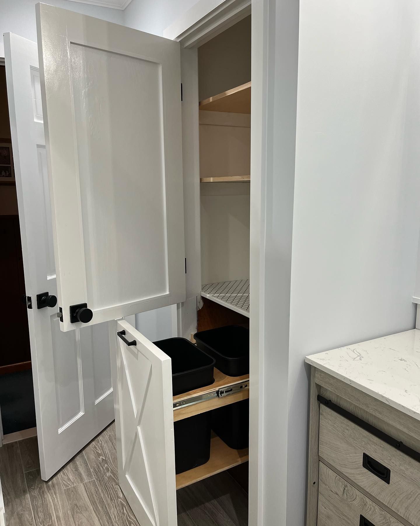 Open pantry cabinet with shelves and a wire basket, next to a countertop drawer unit.