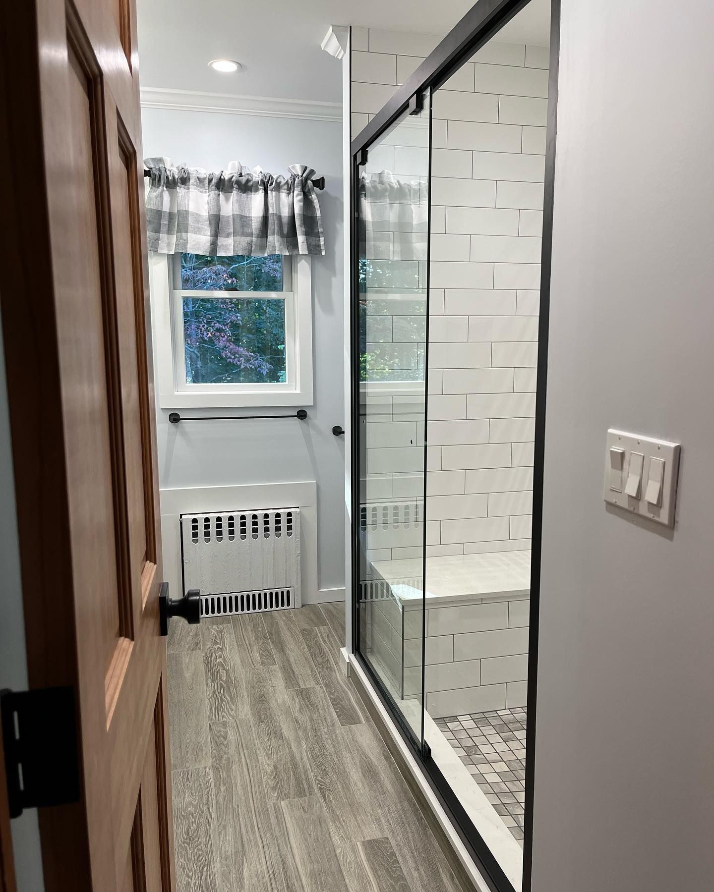 Narrow hallway with wood floor, window, radiator, and a glass shower enclosure on the right.