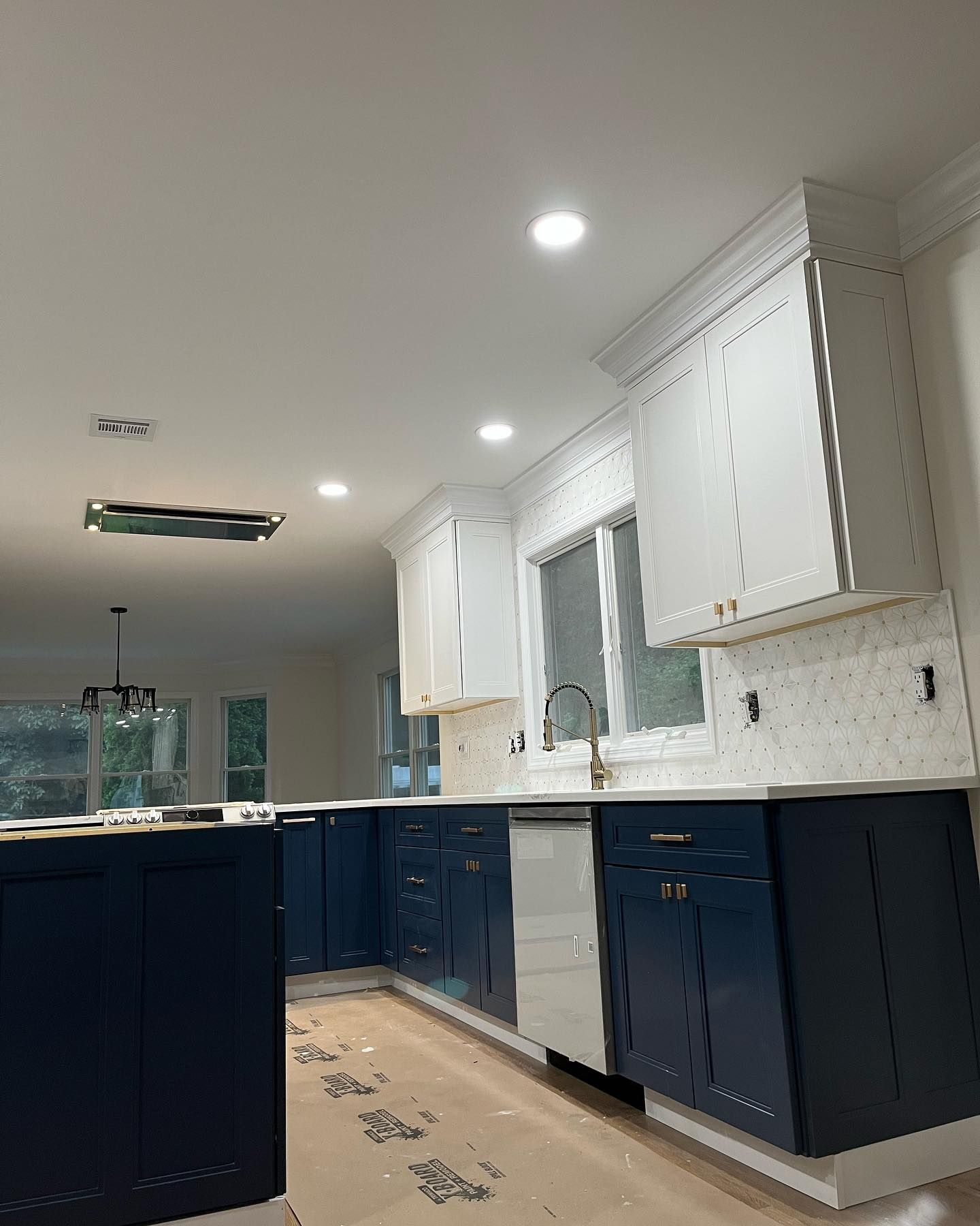 Modern kitchen with navy lower cabinets, white uppers, marble backsplash, and recessed lighting