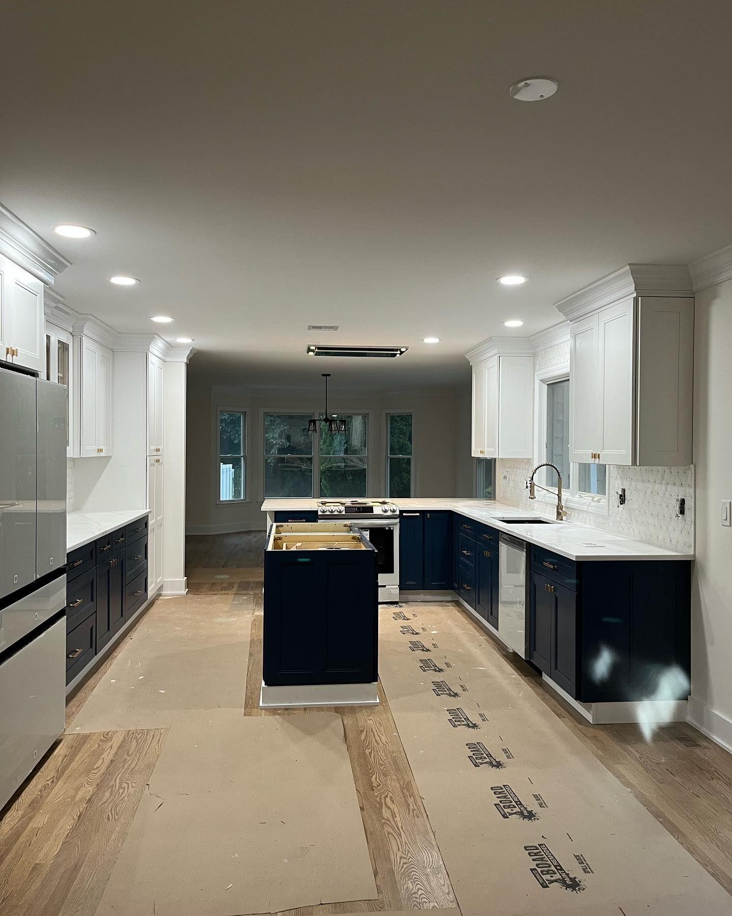 Modern kitchen under renovation with white cabinets, dark island, and protective flooring coverings