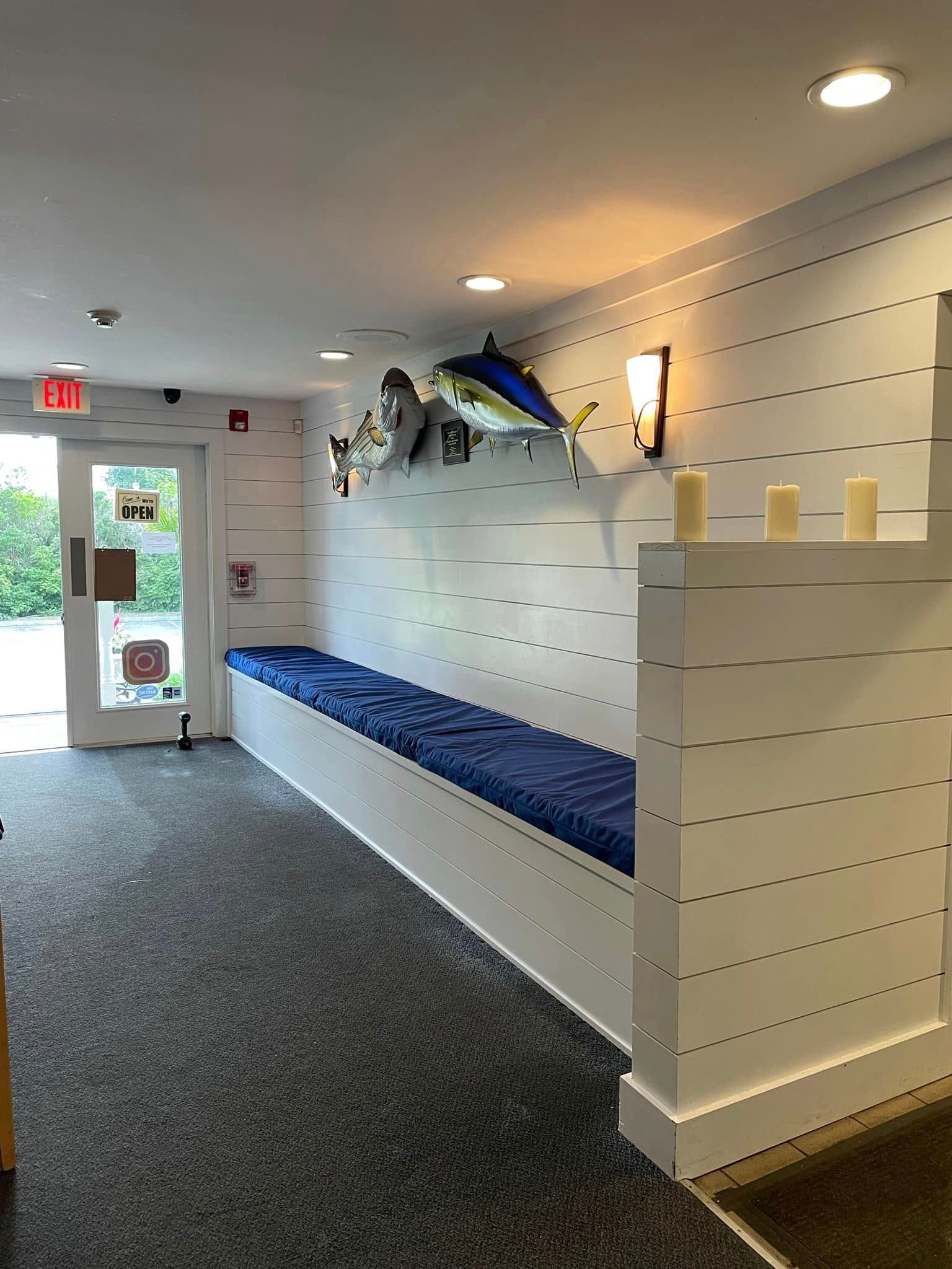 White retail hallway with blue bench, slatwall display, hanging fish decorations, and glass exit door
