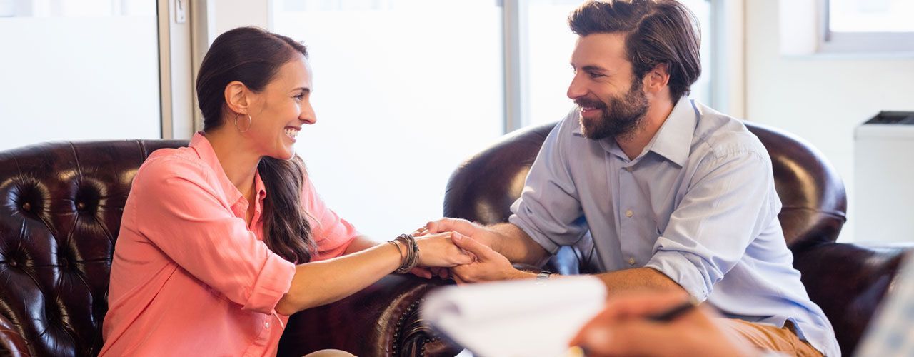 A man and a woman are shaking hands while sitting on a couch.
