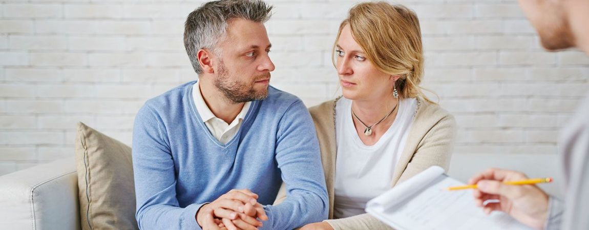A man and a woman are sitting on a couch talking to a therapist.