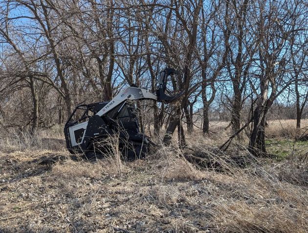 Overturned black machine in dry brush among leafless trees