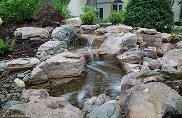 A small waterfall is surrounded by rocks in a garden.