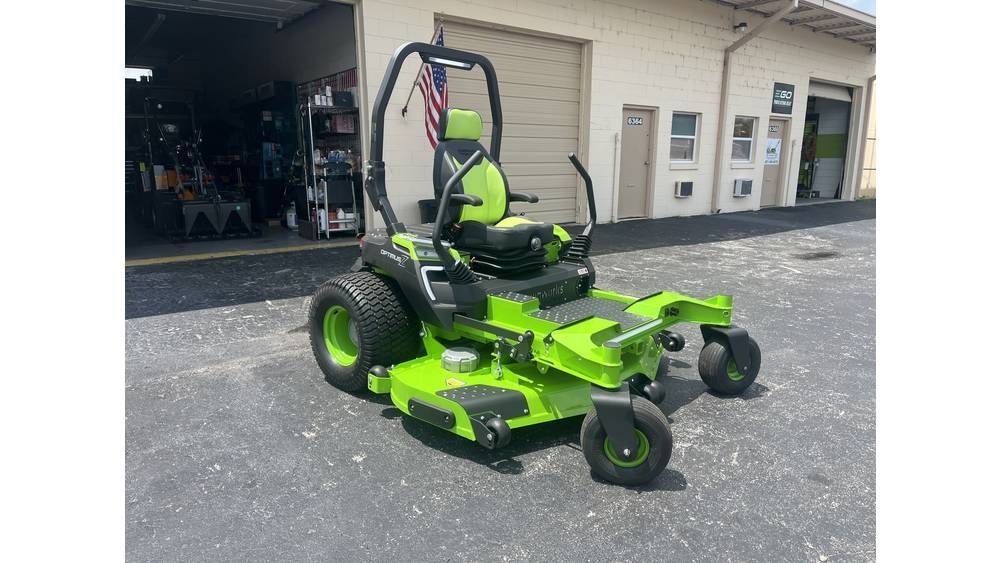 A black pickup truck tows a flatbed trailer loaded with two red Toro construction machines on a paved lot.