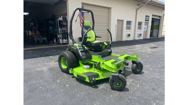 A black pickup truck tows a flatbed trailer loaded with two red Toro construction machines on a paved lot.