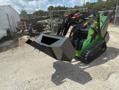 A black metal skid steer grapple attachment with hydraulic hoses, resting on an asphalt surface.
