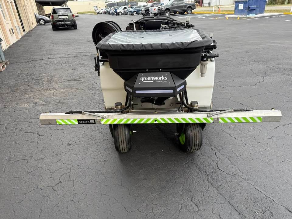 A commercial fertilizer spreader with a green-and-white reflective boom attachment, parked on an asphalt lot.