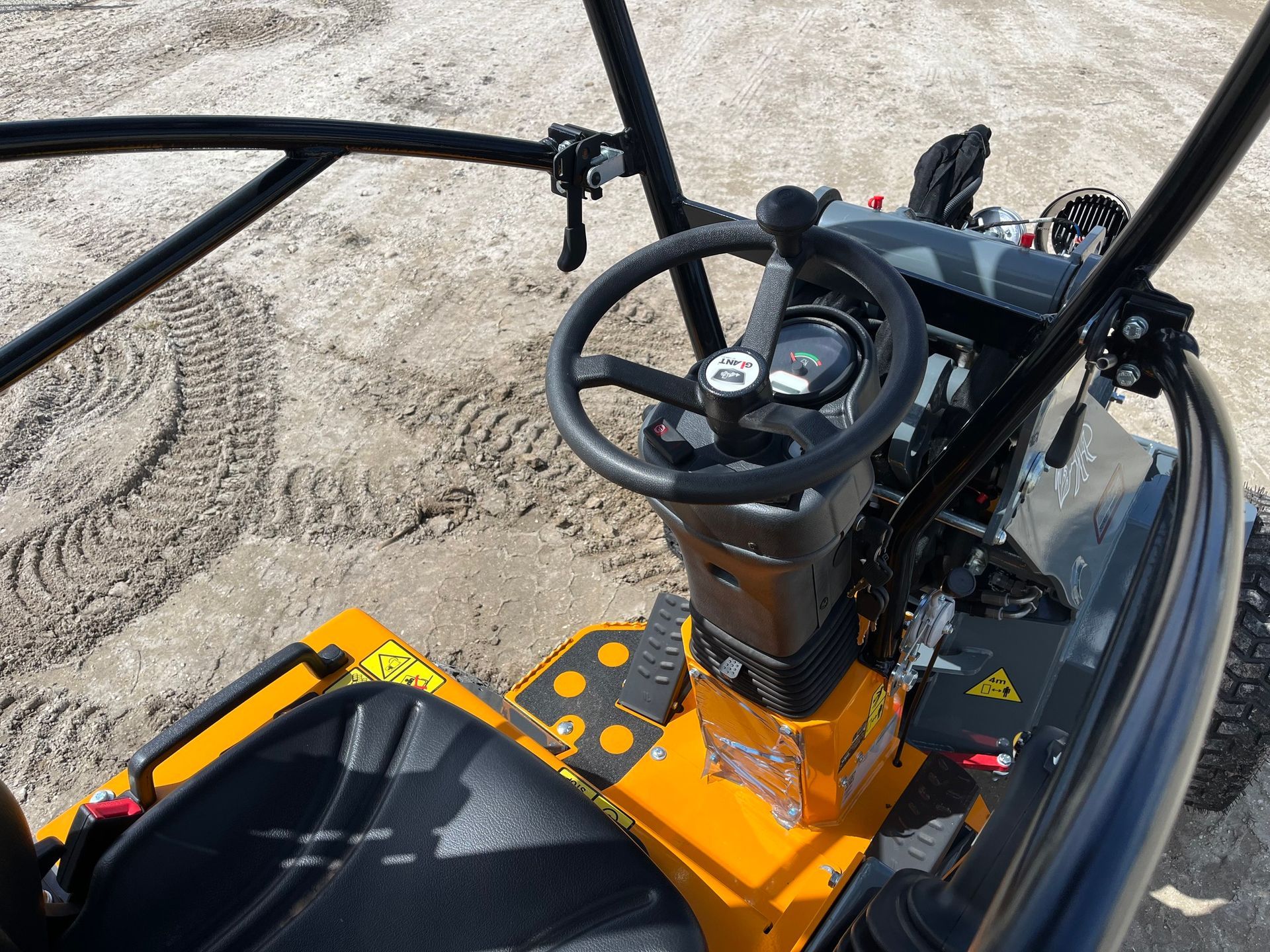 High-angle view of the operator station of a yellow industrial machine, showing a steering wheel, seat, and roll cage.