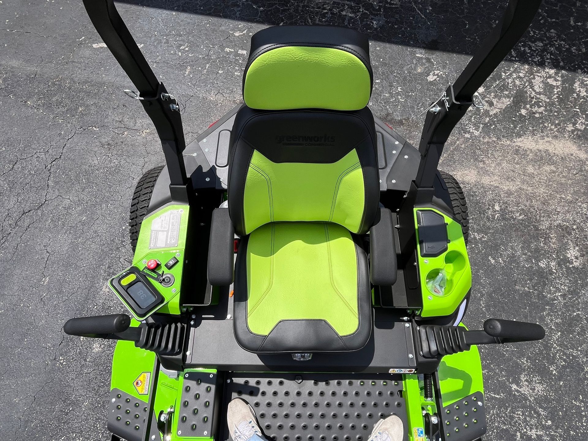 A top-down view of a neon green and black zero-turn lawn mower seat with control levers and foot pedals.
