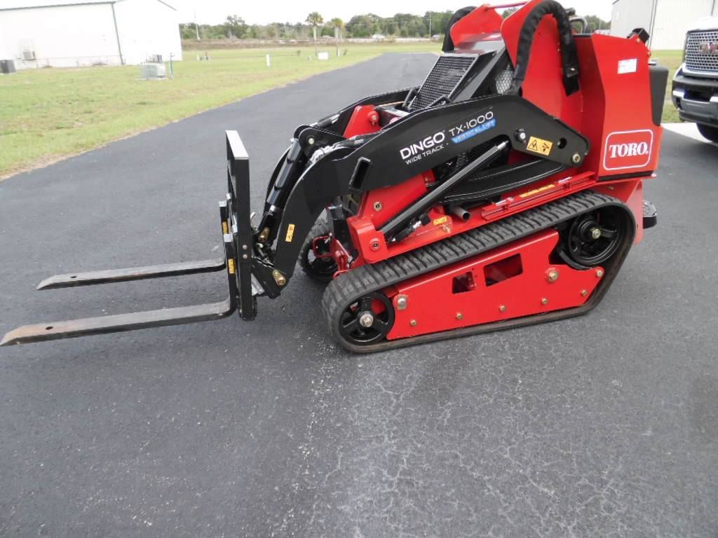 A red Toro Dingo compact track loader with fork attachments parked on an asphalt surface.