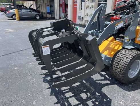 Black grapple attachment on a yellow skid steer in a parking lot