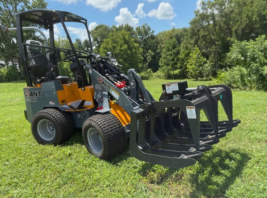Black and orange skid steer loader with grapple bucket on grass under a sunny sky