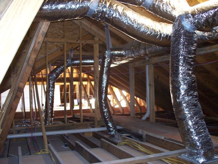 Insulated flexible air ducts running through the wooden framing of an unfinished attic.