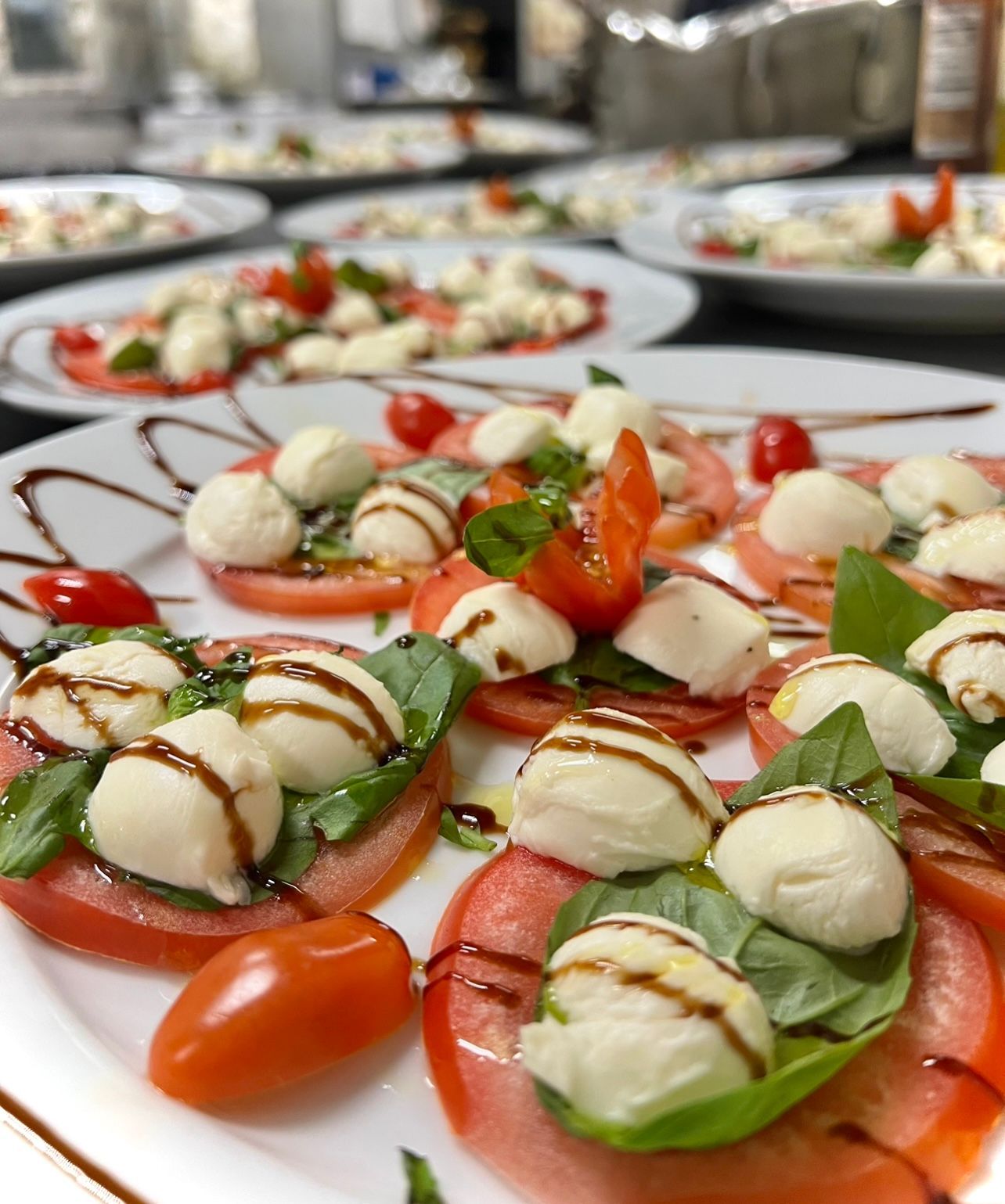 Caprese salad with tomatoes, mozzarella, basil, balsamic glaze on multiple plates.