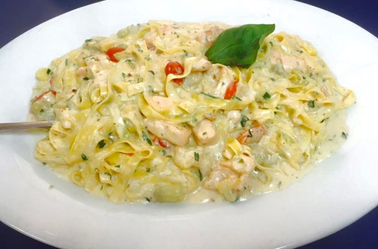 Fettuccine Alfredo with shrimp and tomatoes, garnished with basil, served on a white plate.