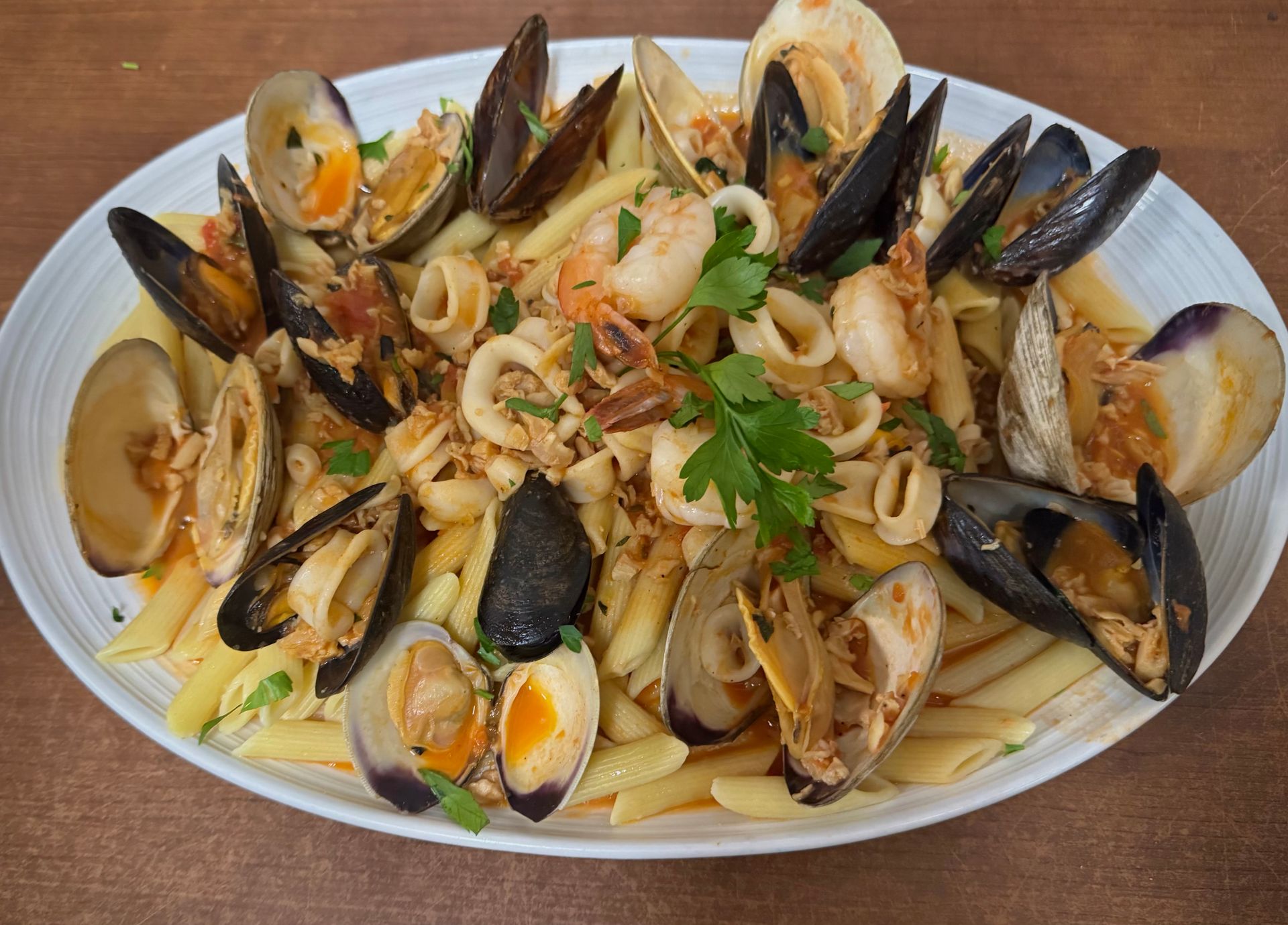 Seafood pasta dish: Penne with clams, mussels, shrimp, and squid in a tomato sauce on a white plate.