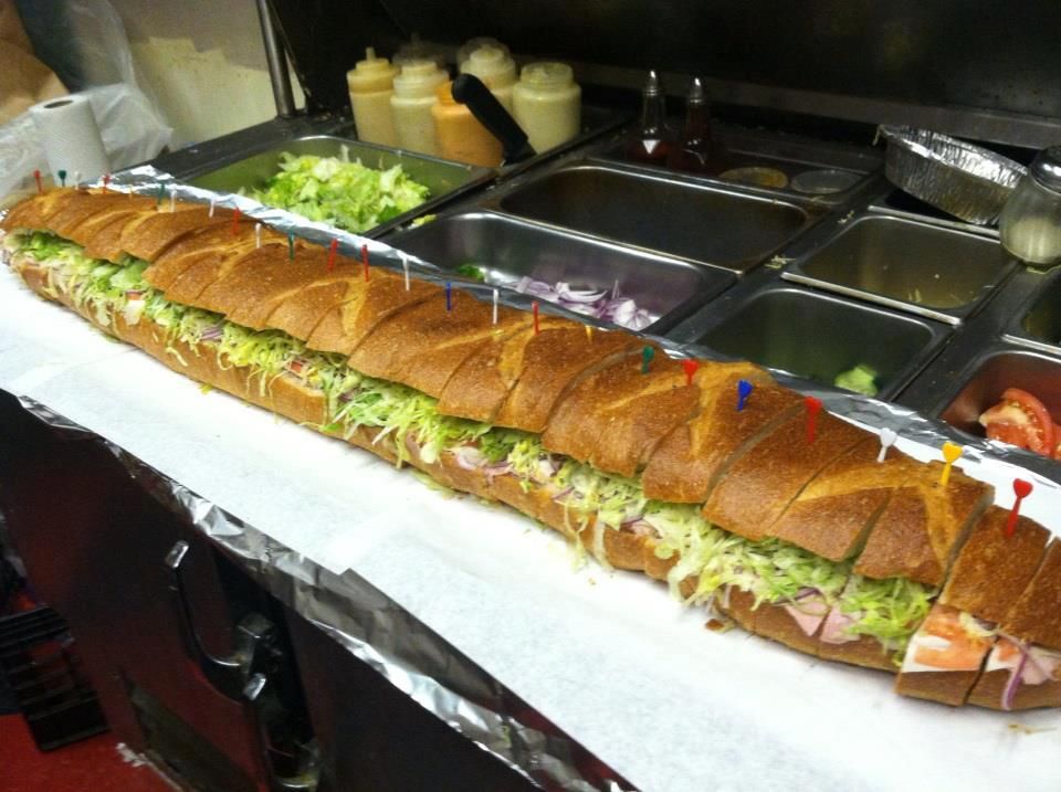 Giant submarine sandwich on a counter, lettuce and toppings visible, ready to be served.