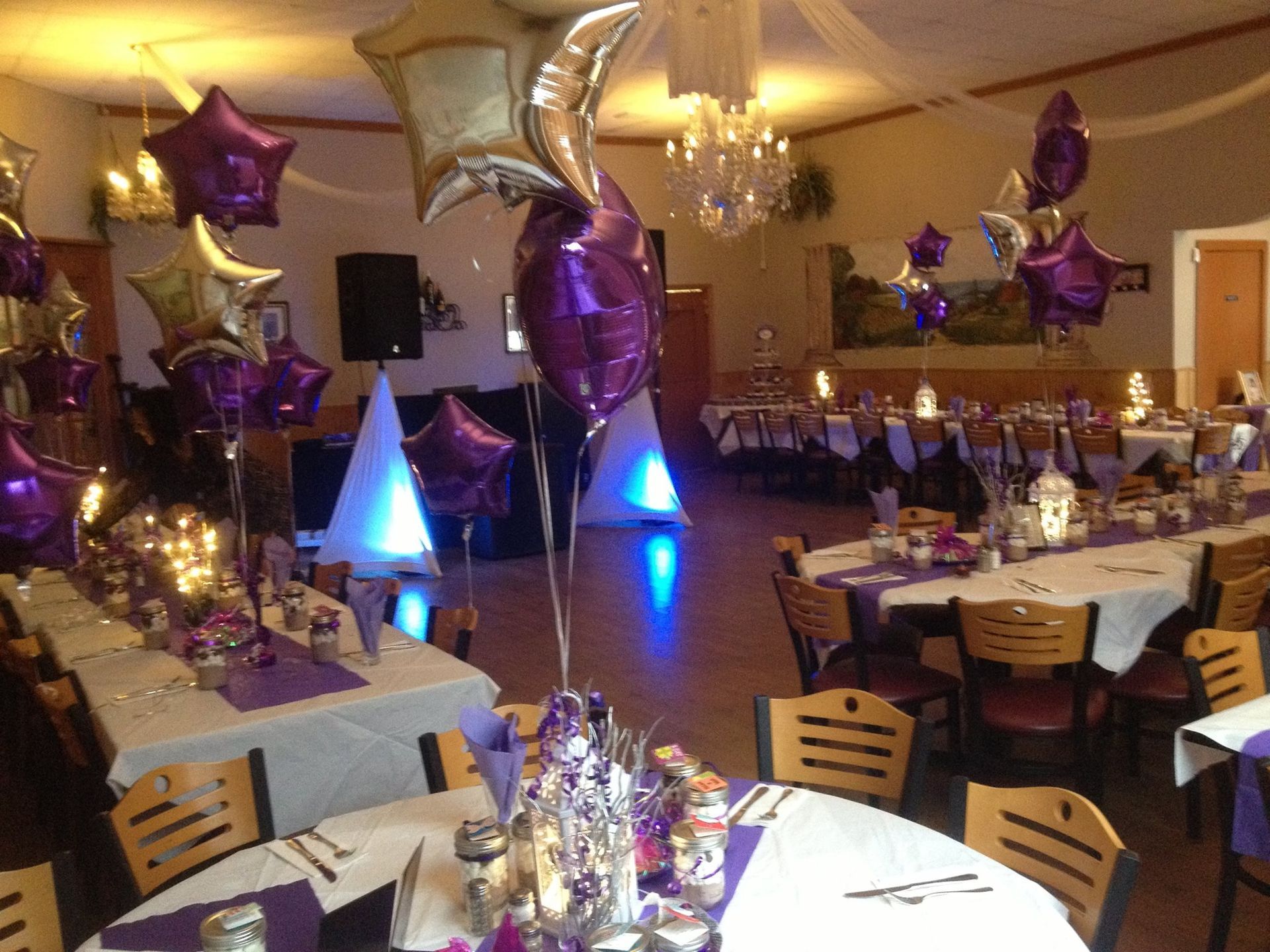 A decorated banquet hall with purple and silver balloons, tables, and lighting.