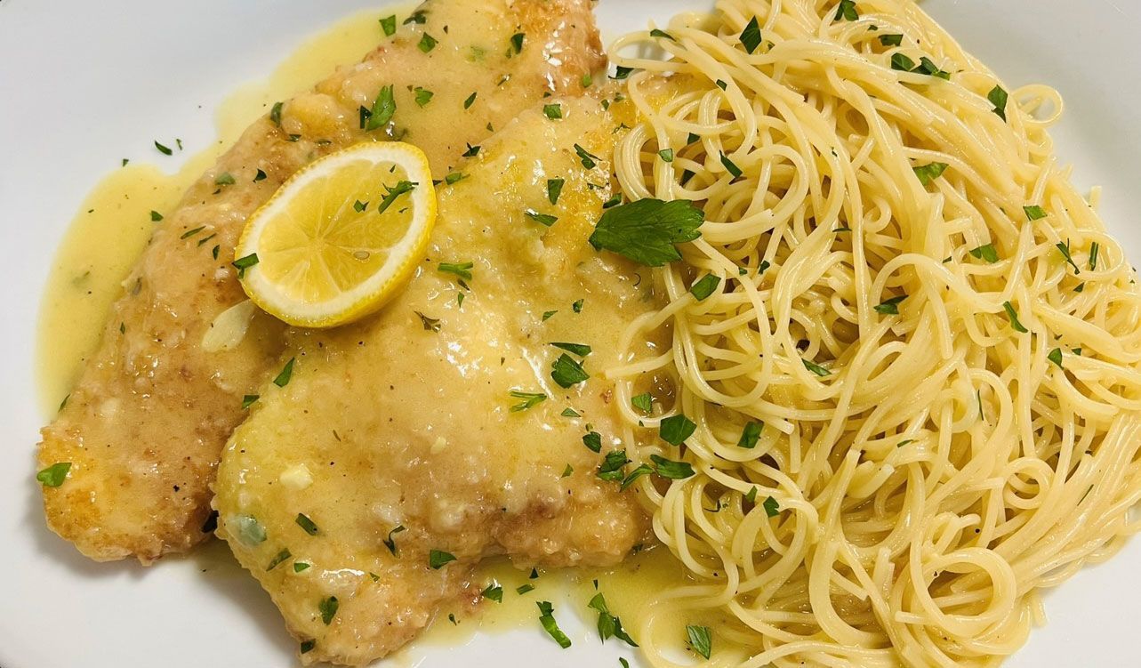 Fish with lemon sauce and spaghetti, garnished with parsley and lemon slice.