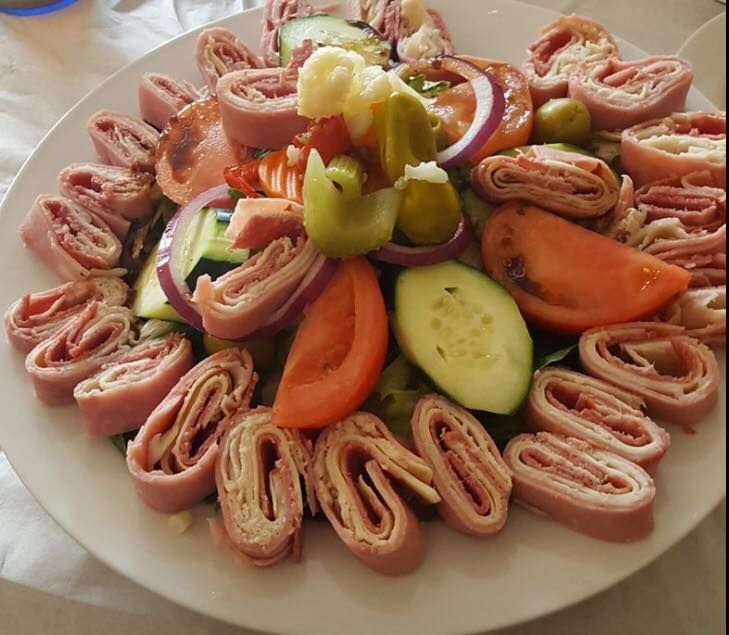 A colorful salad on a white plate with rolled meat, tomatoes, cucumbers, olives, and red onion.